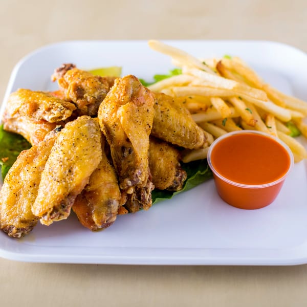 House of Wings' golden-brown wings with black pepper, french fries, and a side of red sauce.