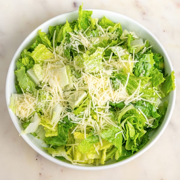A white bowl filled with fresh green romaine lettuce and shredded Parmesan cheese.