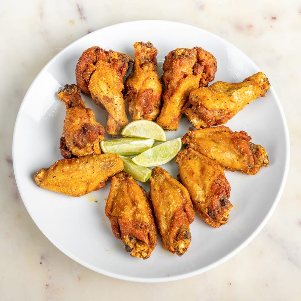 A white plate filled with golden-brown chicken wings and lime wedges on a marble surface.