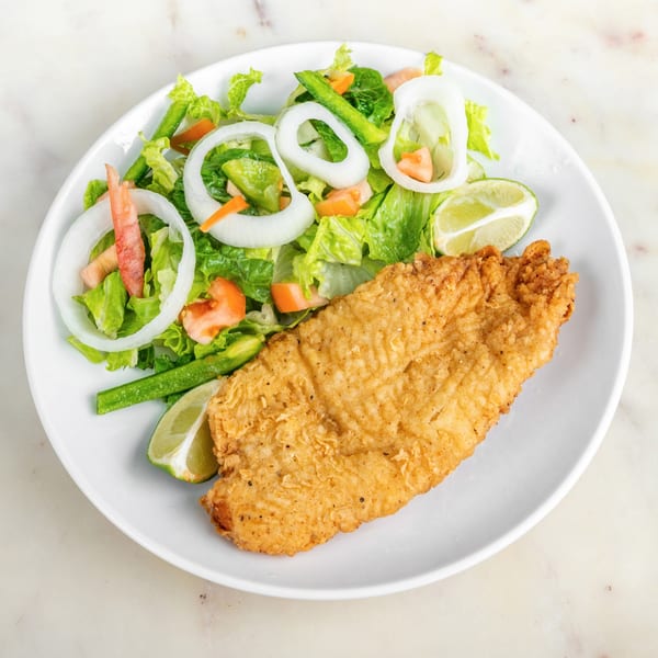 Crispy fried fish fillet with a fresh green salad, onion rings, and lime wedges on a white plate.