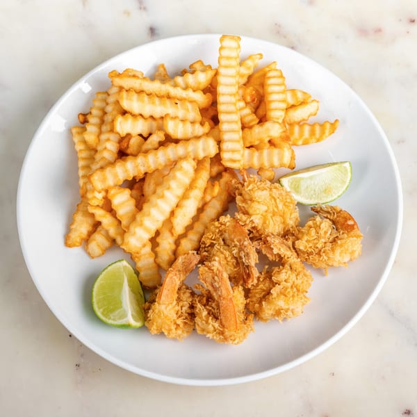 Crispy fried shrimp and crinkle-cut fries with lime wedges on a white plate.