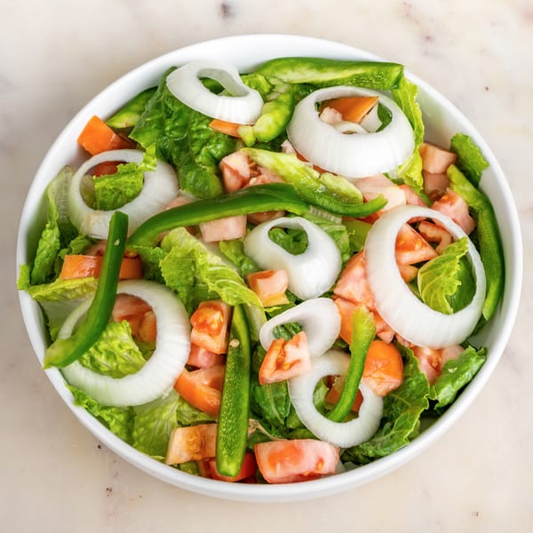 Fresh House of Wings side salad with lettuce, tomatoes, green peppers, and onion rings in a white bowl.