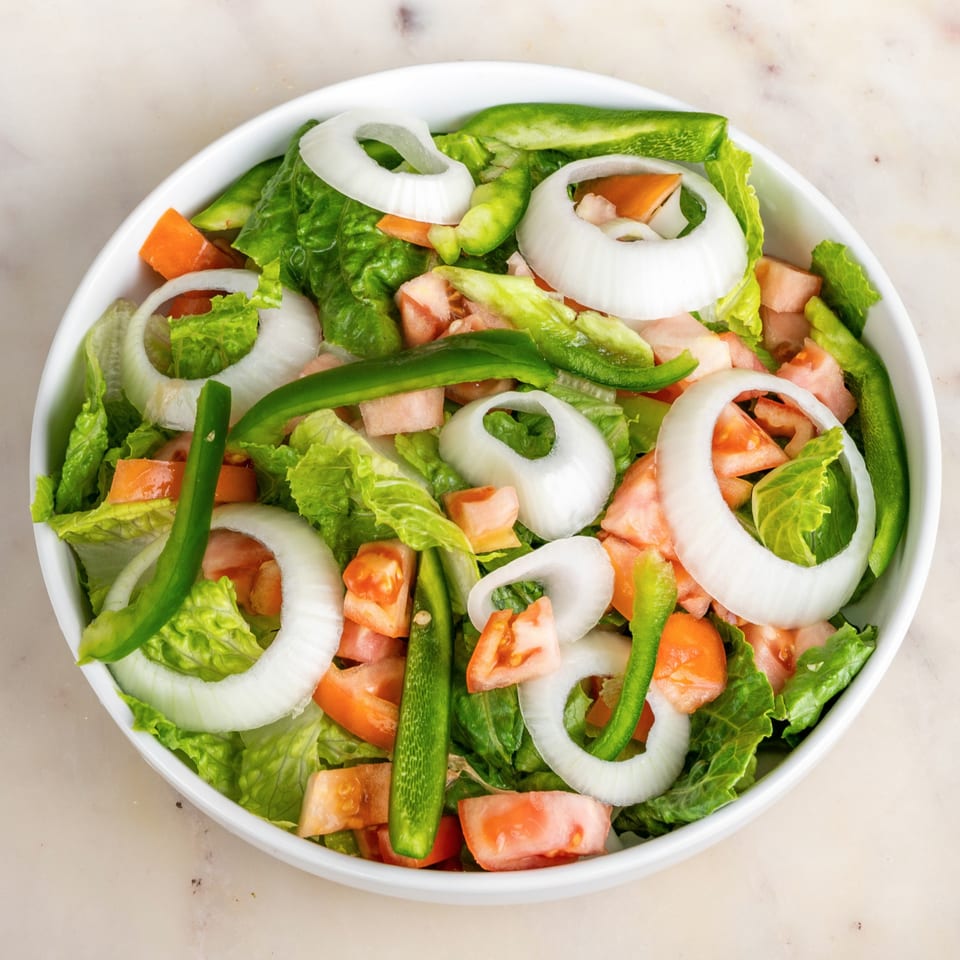 Fresh House of Wings side salad with lettuce, tomatoes, green peppers, and onion rings in a white bowl.