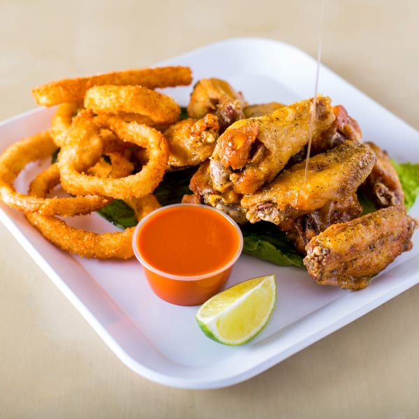 A plate of House of Wings' crispy onion rings and saucy chicken wings, with a side of hot sauce and lime.
