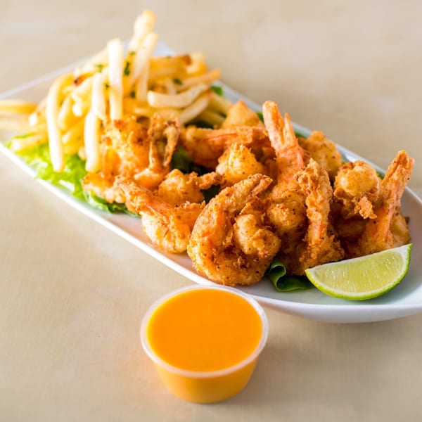 Crispy fried shrimp and french fries on a white plate with a lime wedge and dipping sauce.
