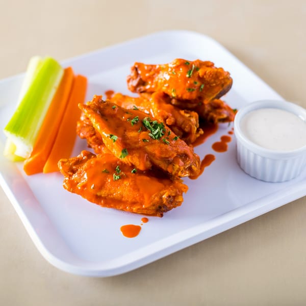 House of Wings' buffalo wings, with celery, carrots, and ranch dressing on a white plate.