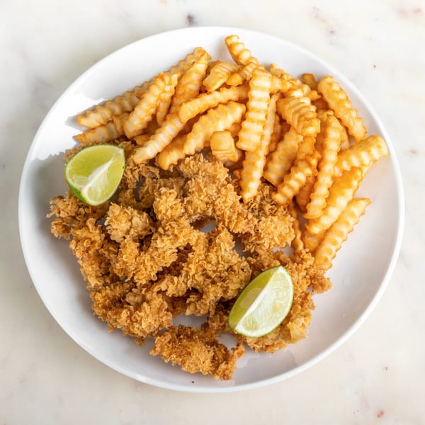 Crispy fried chicken tenders and crinkle-cut fries with two lime wedges on a white plate.