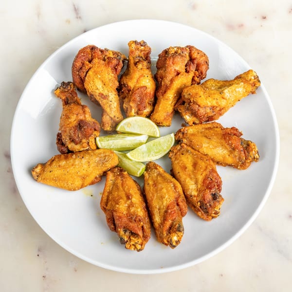 A white plate filled with golden-brown chicken wings and lime wedges on a marble surface.